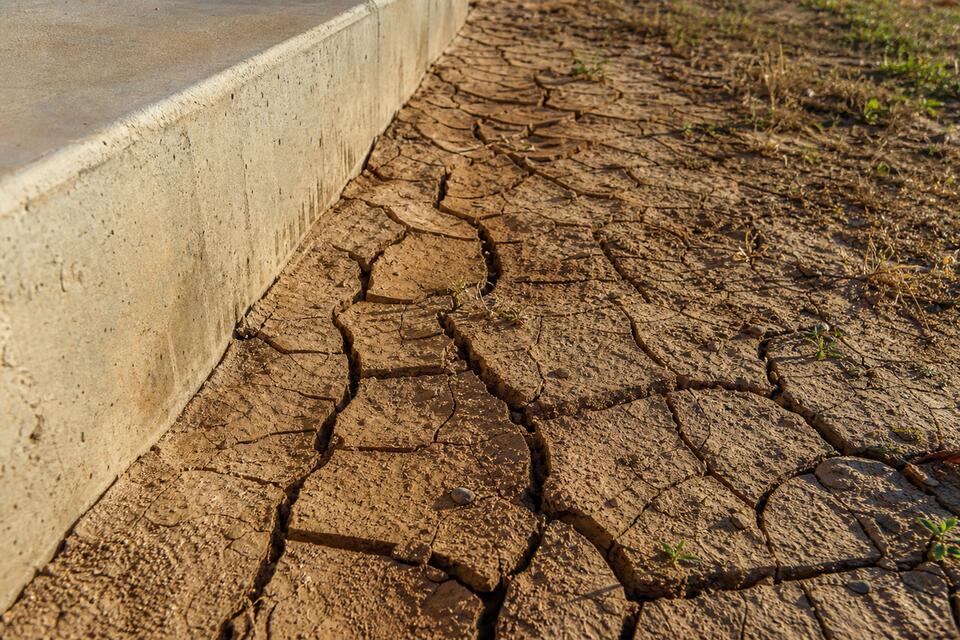 Expansive clay soil cracking beside a concrete slab foundation in San Antonio